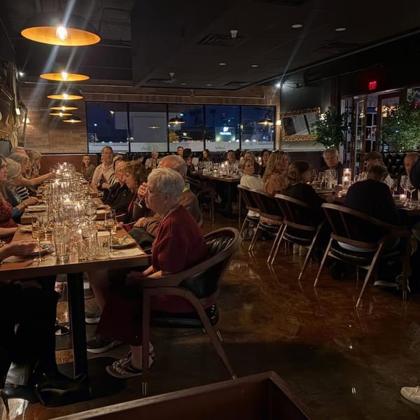 Diners seated at long tables in a dimly lit restaurant with warm overhead lighting and candles.