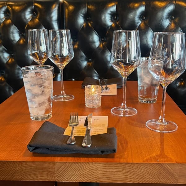 A set table with wine glasses, water glasses, silverware, and a lit candle against a dark tufted booth.