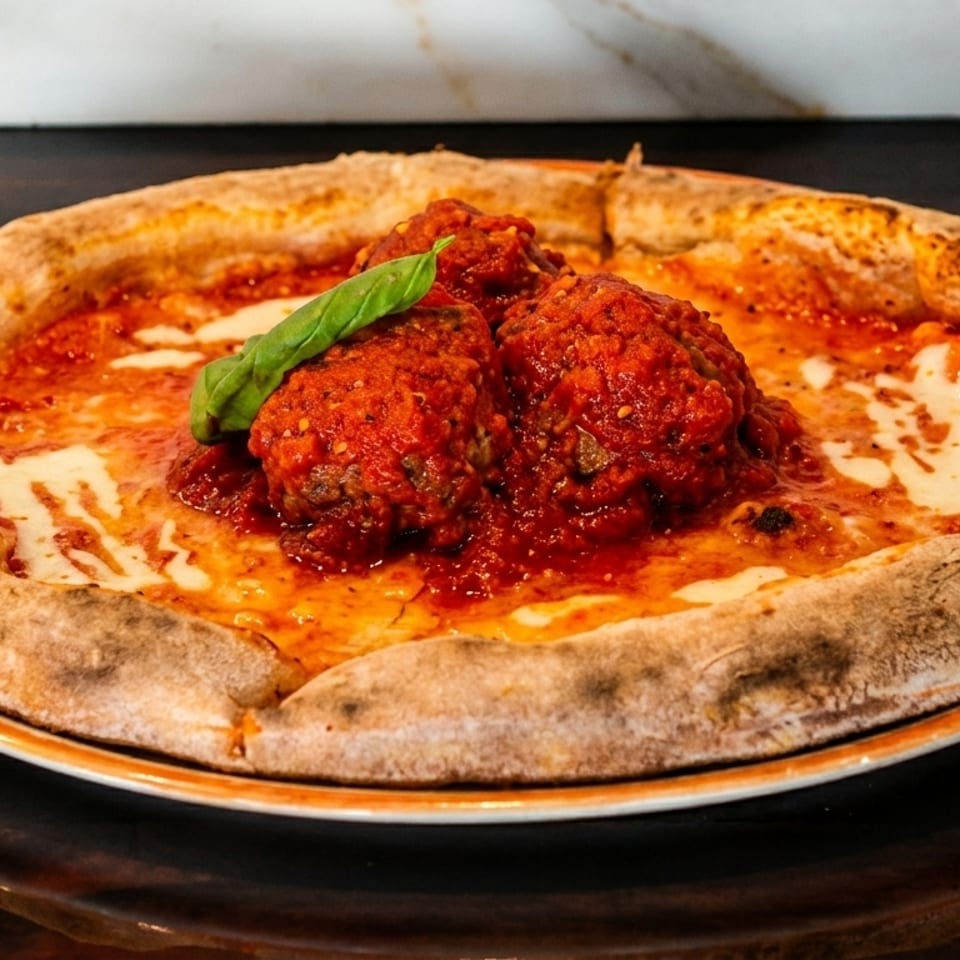 Meatball pizza with rich red sauce, melted mozzarella, and fresh basil on a rustic crust.