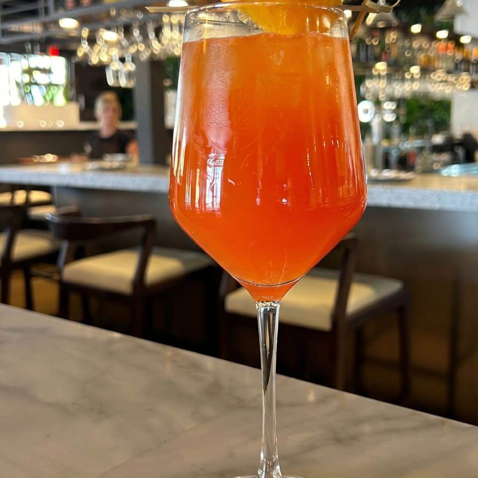 An orange cocktail with an orange slice garnish sits on a marble bar top.